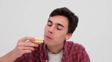 Erkek, kararlı ama tatmin olmuş bir ifadeyle temiz beyaz bir arka fonun karşısında pizzanın tadını çıkarıyor, her bir lezzetli lokmayı taze bira yudumuyla yıkıyor..