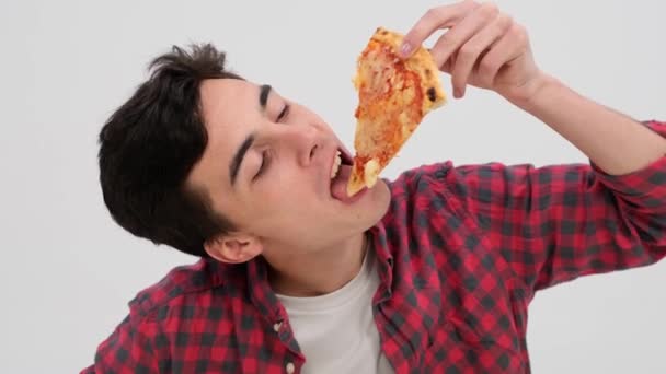 白人男性はピザの味を和らげ 純粋な楽しみを反映した表現をしています きれいな白い設定の背景に対して 彼は噛み チーズ ソース および地殻のブレンドを味わう — ストック動画