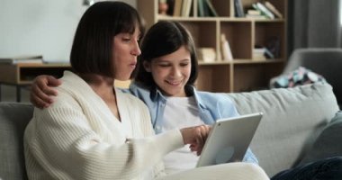 Anne ve oğlu oturma odasında keyifli vakit geçiriyorlar, tablet bilgisayar kullanarak ve kahkahalarını paylaşarak. Onların neşeli etkileşimleri odaya bir beraberlik ve neşe katar..