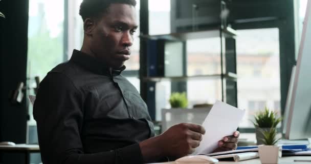 アフリカ系アメリカ人の起業家は オフィスのコンピュータで働いている間 書類の処理に熱心に取り組んでいます このシーンは 管理タスクと事業運営へのコミットメントを示しています — ストック動画
