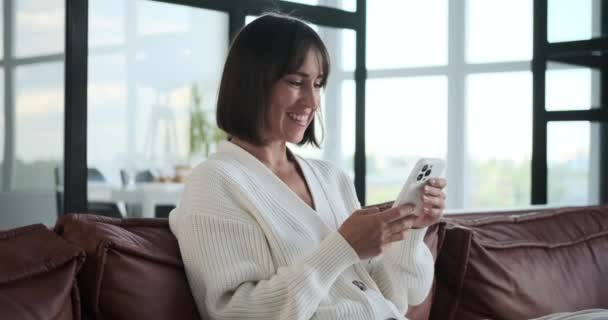 Gülümseyen Beyaz Kadın Telefon Kullanırken Koltukta Dinleniyor Onun Neşeli Ifadesi — Stok video
