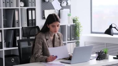 Profesyonel ofis ortamında, genç beyaz bir kadın özenle belgelerle çalışıyor, kurumsal çevreye bağlılığını ve konsantrasyonunu sergiliyor..