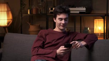 Kanepede telefonla uğraşırken neşeli beyaz bir adam gülüyor. Sahne, evdeki rahatlığı yansıtan neşeli bir mizah ve bağlantı anı yakalıyor..