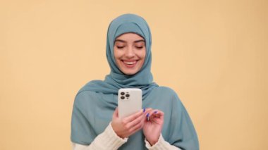 Neşeli bir iletişim anında, gülen bir Arap kadın telefonda canlı mesajlaşır, rahatlatıcı bir bej arka plana mutluluk saçar, canlı ve neşeli bir sahne yaratır..