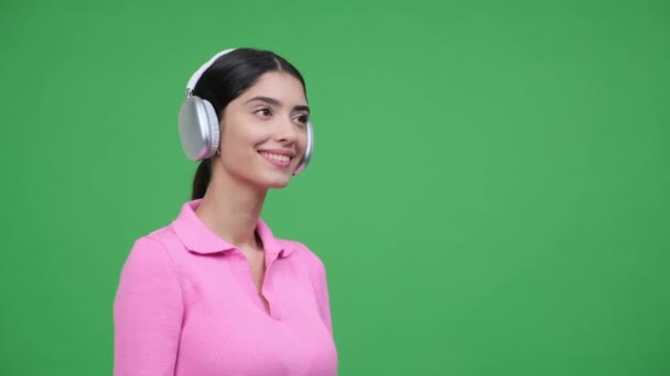 人们把带着欢乐笑容的女人刻画在侧面 通过耳机欣赏音乐 静谧的绿色背景场景展现了积极和沉醉的音乐体验的乐趣 — 图库视频影像