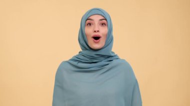 Coşkulu bir Arap kadını, sıcak bir bej arka planda hayranlığını dile getiriyor. Pozitif enerjiyle dolu bir sahnede saf neşe ve hayranlık dolu bir anı yakalıyor..