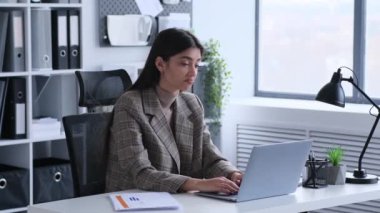 Beyaz bir kadın ofiste dizüstü bilgisayarla çalışırken omuz silkiyor. Bu resim profesyonel görevlerin zorluklarına eşlik eden nüanslı duygu ve jestleri yakalar..