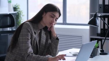 Can sıkıntısı çeken bir iş kadını, iş sırasında ofis masasında oturur. Bu görüntü, onun hissettiği bağlılık eksikliğini ve monotonluğu yansıtıyor ve odak ve ilgiyi koruma zorluklarını vurguluyor..