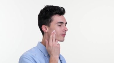 Adam cildine nazikçe yüz kremi sürüyor, sakin ve odaklanmış ifade ediyor. Parmakları yavaş, kasıtlı daireler çiziyor, hassas bir şekilde besleniyor..