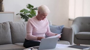 Bilge ve deneyimli yaşlı kadın detaylara dikkat ederek kağıtlarla çalışıyor. Doğal ışığın yumuşak parıltısıyla çevrelenmiş halde, belgeleri hassasiyetle ve dikkatle tutuyor..