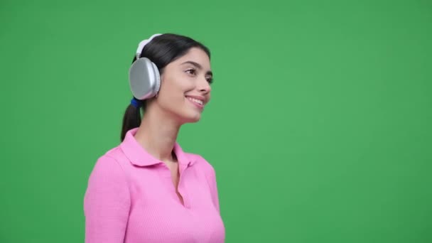 一个女人带着耳机 沉浸在音乐的喜悦中 在绿色的背景下被拍了下来 她灿烂的微笑反映出曲调的欢愉 营造出和谐欢乐的气氛 — 图库视频影像