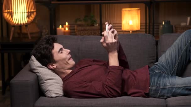 Junger Erwachsener Mann Liegt Auf Dem Sofa Und Spielt Mit — Stockvideo