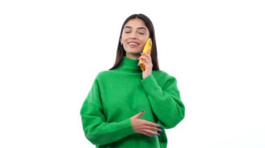 Genç bir kadın neşeli bir telefon görüşmesi yapıyor, temiz beyaz bir arka plana pozitif titreşimler yayıyor. Bu görüntü iletişimin neşesini yakalar. .