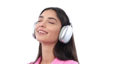Kafkasyalı kadın müziğin tadını çıkarıyor, kulaklık takarken ritmin içinde kayboluyor, dingin beyaz bir arka plana karşı. Bu görüntü, keyifli müzik düşkünlüğünün özünü yakalar. .