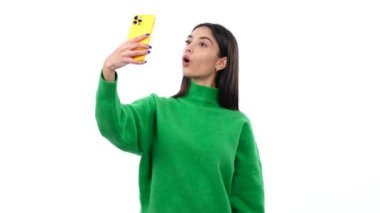 Kafkasyalı bir kadın temiz beyaz bir arka planda selfie çekiyor. Bu canlı görüntü neşe ve spontanelik yayar, kendini ifade etme sevincini aktarmak için mükemmeldir..