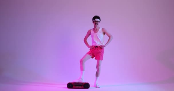カリスマ的なコーカサス人男性は口ひげで飾られ 魅惑的な紫色の背景に対する古典的なカセットプレーヤーと一緒にエキゾチックな踊り この活気あふれるシーンはレトロな精神を捉えています — ストック動画