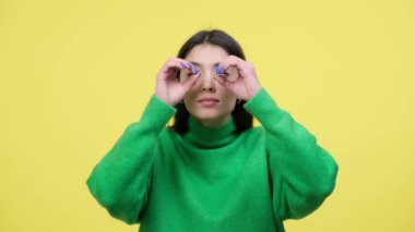 Şaşırmış, beyaz bir kadın el dürbününü gözlerine tutarak şaşkınlık ve merak hissini dile getiriyor. Sarı arka plan görsel bir ilgi uyandırır, keşif ve merak anı yaratır..