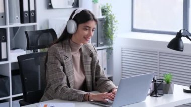 Kulaklıklı iş kadını ofiste çalışırken müziğin tadını çıkarıyor. Bu resim, onun mesleki rutinine dahil ettiği pozitif ve zevkli anları yakalıyor..