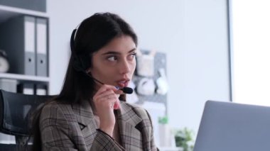 Müşteri desteği temsilcisi ofiste kulaklık ve dizüstü bilgisayarla iletişim kuruyor. Bu görüntü, onun yardım sağlarken aldığı profesyonel ve özenli yaklaşımı yakalar..