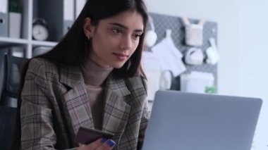 Odaklanmış beyaz kadın, ofisteyken kredi kartıyla online alışveriş yapıyor. Bu resim molada kişisel görevlerin yönetilmesinin kolaylığını yakalar.