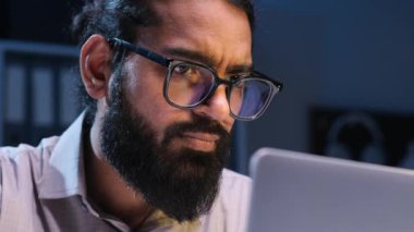 Yoğunlaşmış işadamı özenle bir dizüstü bilgisayarla çalışırken yakalandı. Profesyonelce giyinmiş, odaklanmış ifadeler gece görevleri sırasında kendini adamışlık ve yoğunluğu ifade eder..