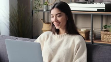 Beyaz bir kadın dizüstü bilgisayarla koltukta otururken canlı bir video görüşmesi yapıyor. Bağlı kalmanın modern özünü aktarıyor. Evin rahatlığı mutluluk için bir zemin haline geliyor..