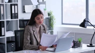 Kafası karışık genç iş kadını bürodaki belgelerle uğraşırken omuz silkiyor. Bütçeyi gözden geçir, tepkiler karışık.