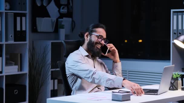 快乐的印度男性员工在智能手机上聊天 在晚上的办公室里大笑 休息期间的放松 懒散的电话交谈 远程通信 — 图库视频影像