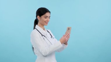 Pozitif kadın doktor mavi arka planda telefon kullanıyor. Teknoloji ve sağlık karışımı, çevrimiçi tıbbi servis, modern tıp, tıbbi personel kavramı.