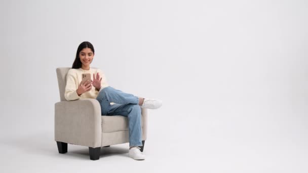 Pozytywna Biała Kobieta Telefonem Wskazuje Palcem Prawo Siedząc Fotelu Białym — Wideo stockowe