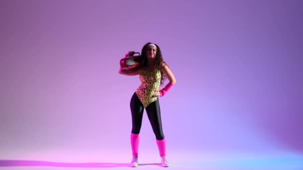 レトロアンサンブルのネルディーな女性は 活気に満ちた紫色の背景で踊ります 手を握り 古典的なブームボックス レトロエネルギーのバーストで大気を増幅 — ストック動画