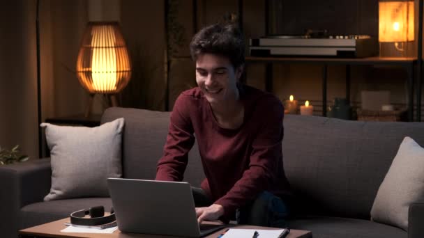 ポジティブで笑顔のコーカサス学生や従業員は 夜のリビングルームのソファーで仕事やリモート研究のためにノートパソコンを使用しています オンライン学習 デジタル教育 Eラーニングコンセプト — ストック動画