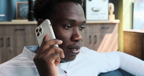 笑着的非裔美国人 穿着白衬衫的商人坐在沙发上和电话交谈 远程联系 人们的生活方式 与朋友 同事或客户交谈的概念 — 图库视频影像