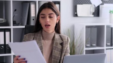 Modern ofiste çalışan kadın girişimci, video görüşmesi sırasında konuşan, dizüstü bilgisayar kullanan, evrak işi yapan, muhasebe işi yapan, uzaktan iletişim kuran..