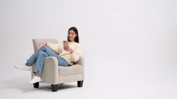 Jovem Sorridente Usa Telefone Enquanto Senta Uma Poltrona Para Comunicação — Vídeo de Stock