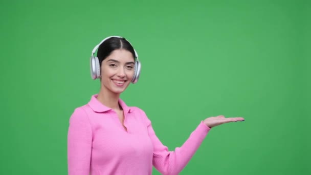 Χαρούμενη Καυκάσια Νεαρή Γυναίκα Φορώντας Ακουστικά Που Δείχνουν Δεξιά Παλάμη — Αρχείο Βίντεο