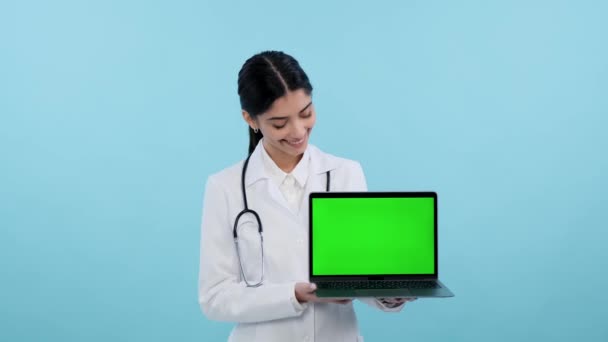 身穿医用童装的微笑医生或护士拿着带有绿色屏幕的笔记本电脑在蓝色背景上做广告 设备筛选 医学和技术概念的混合 — 图库视频影像