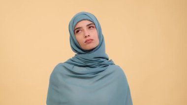Düşünceli, tesettürlü Müslüman kadın etrafa bakıyor, beyin fırtınaları yapıyor ve bej bir arka plan yansıtıyor. Bir çözüm bulunca, kadın şüphe eder, düşünür ve planlar yapar..