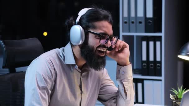 Tyytyväisen Intialaisen Liikemiehen Muotokuva Kuulokkeissa Kuuntelemassa Musiikkia Yötoimistossa Hymyilevä Mies — kuvapankkivideo