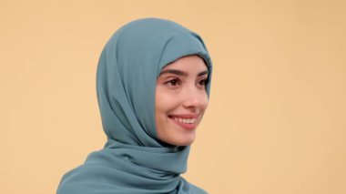 Bej bir arka planda duran ve gülümseyen, geleneksel tesettürlü, pozitif bir Arap kadının portresi. Ortadoğu kadınlığı, neşe ve kaygısız ruh hali.