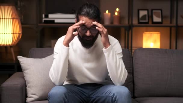 疲れたインド人男性は 自宅で夜の失敗に動揺して頭痛 思慮深いソファーに座って 強調しました バーンアウト 仕事での危機 家族の問題の概念 — ストック動画