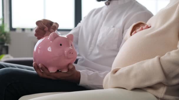 Mann Und Schwangere Frau Legen Münzen Ein Sparschwein Wohnzimmer Geburtsvorbereitung — Stockvideo