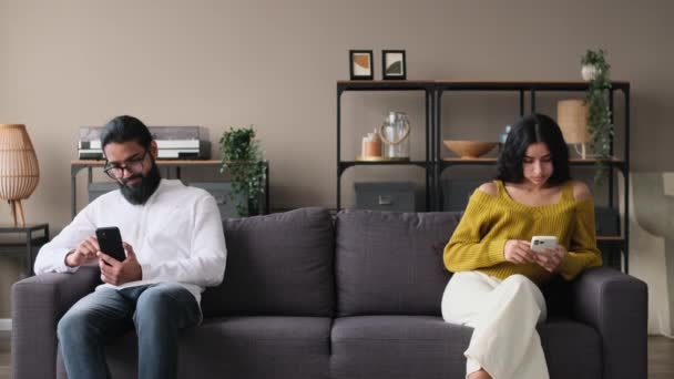 不幸なインド人夫婦は 自宅のソファーに携帯電話で座って互いに怒った 家族関係の問題 紛争と離婚の概念 — ストック動画