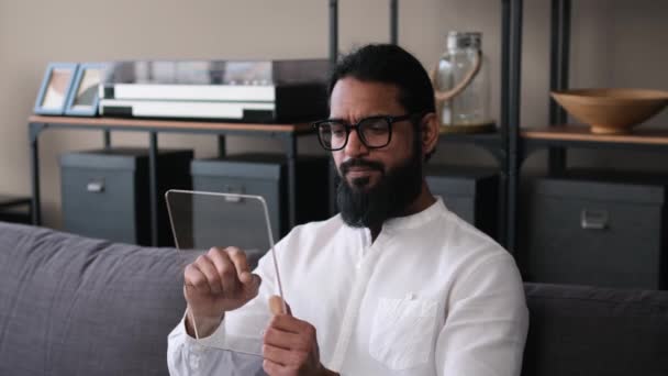自宅で働くために透明なデジタルタブレットを使用して深刻なインドのビジネスマン リモート作業 モダンなガラスタブレットテンプレート デバイス画面モックアップ — ストック動画