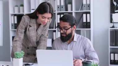 Pozitif ofis çalışanları, Hintli erkek ve Kafkasyalı kadın ofiste dizüstü bilgisayarla konuşup birlikte çalışıyorlar. profesyonel beyin fırtınası ve işbirliği.