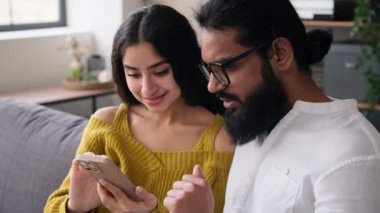 Neşeli Hintli çift telefon kullanıyor, zafere ya da iyi habere şaşırıyorlar, başarıyı beşlikle kutluyorlar. Oturma odasında kanepede dinleniyorum..