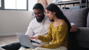 Neşeli aile dizüstü bilgisayarla rahatlıyor ve oturma odasında gülüyor. Birlikte boş zaman geçirmek, internette sörf yapmak, online alışveriş yapmak ya da mesajlaşma kavramı.