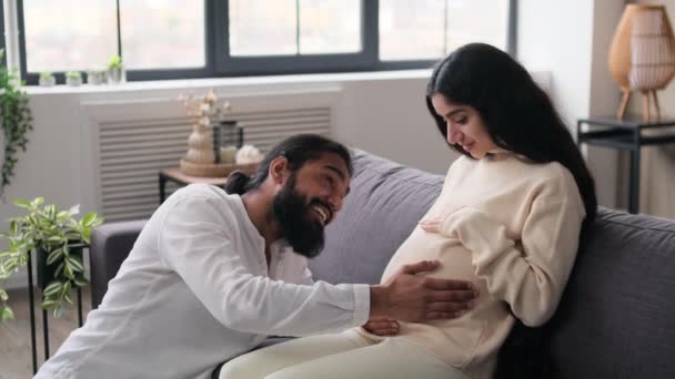 Šťastný Indický Manžel Hladí Ženu Těhotné Břicho Zatímco Sedí Pohovce — Stock video