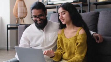 Evli Hintli aile dizüstü bilgisayarlarıyla rahatlıyor ve evde gülüyor. Sosyal medyada sörf, online alışveriş, internette gezinme.