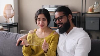 Modern bir tablet bilgisayar kullanarak video görüşmeleri yapan Hintli mutlu bir aile. Oturma odasındaki koltukta dinleniyorlar. dijital tablet şablonu.